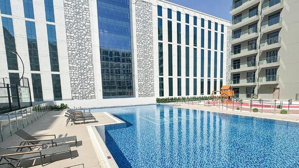 Piscina com espreguiçadeiras, área de recreação infantil e edifícios modernos com amplas janelas e fachada estampada.
