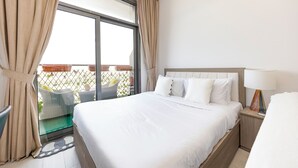 Quarto de hotel com uma cama grande, mesa de cabeceira com abajur, janela com cortinas e vista para a varanda externa.