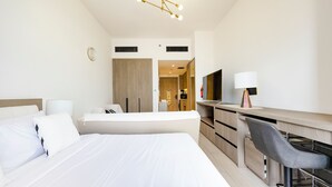 Quarto de hotel moderno com uma cama grande, uma escrivaninha, uma cadeira, uma TV e um candeeiro de teto.