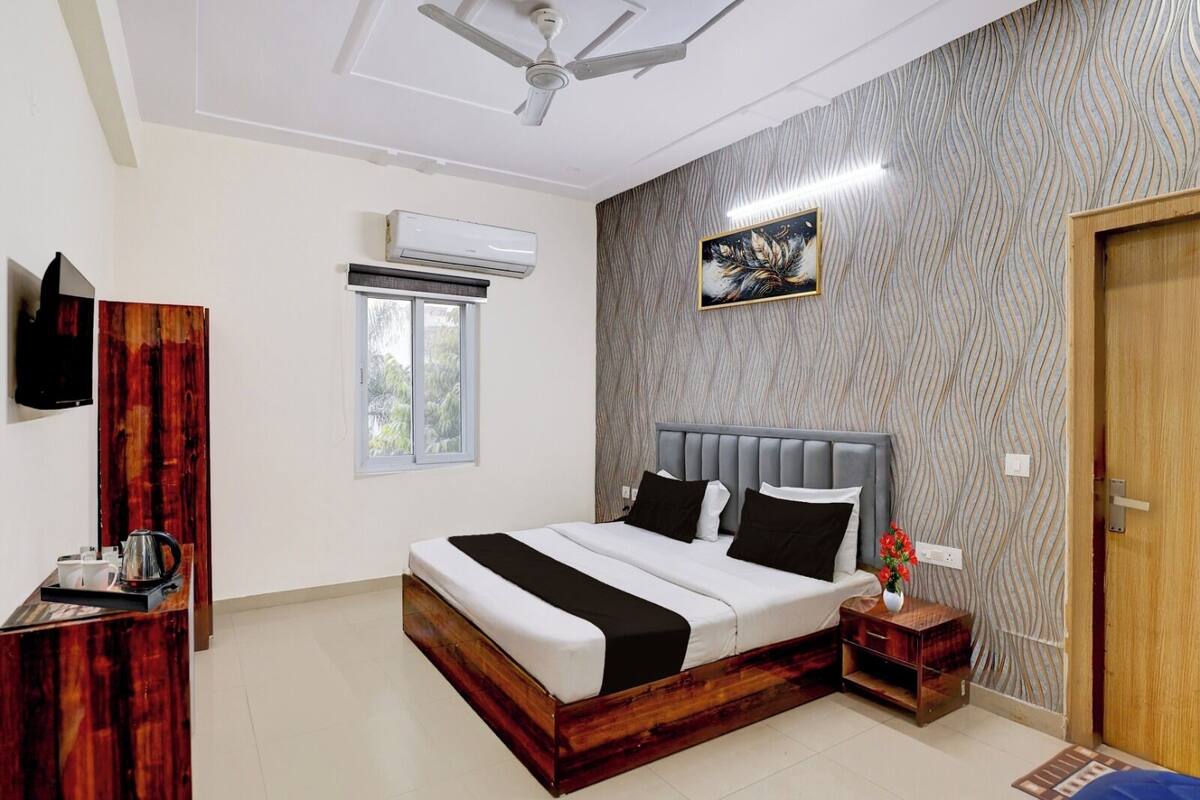 A bedroom with a bed, a ceiling fan, an air conditioning unit, a window, a painting, and a wooden door.