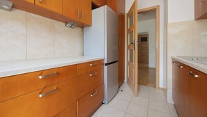 A kitchen with wooden cabinets, a white countertop, and a refrigerator. - Bright Apartment with a Balcony | A Place to Work (Warszawa)
