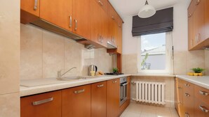 A kitchen with wooden cabinets, a white countertop, a stove, and a window with a view. - Bright Apartment with a Balcony | A Place to Work (Warszawa)