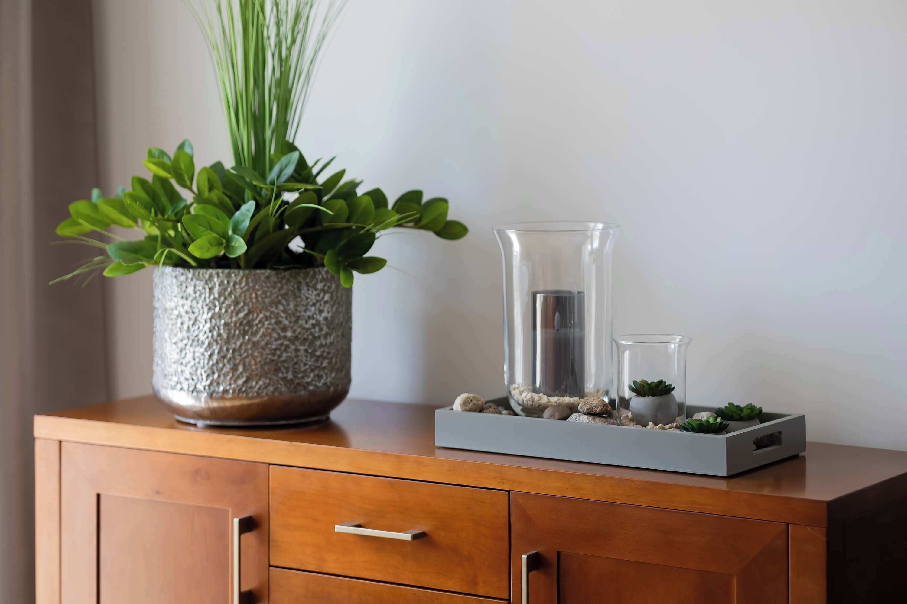A wooden cabinet with a textured pot, a tall glass vase, and a smaller glass container with plants.