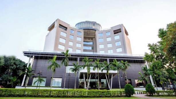 A modern hotel with a central circular atrium, multiple floors, and a well-maintained garden with palm trees. - Holiday Home (Ranchi)