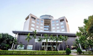 Un hotel moderno con un atrio circular central, varios pisos y un jardín bien cuidado con palmeras.