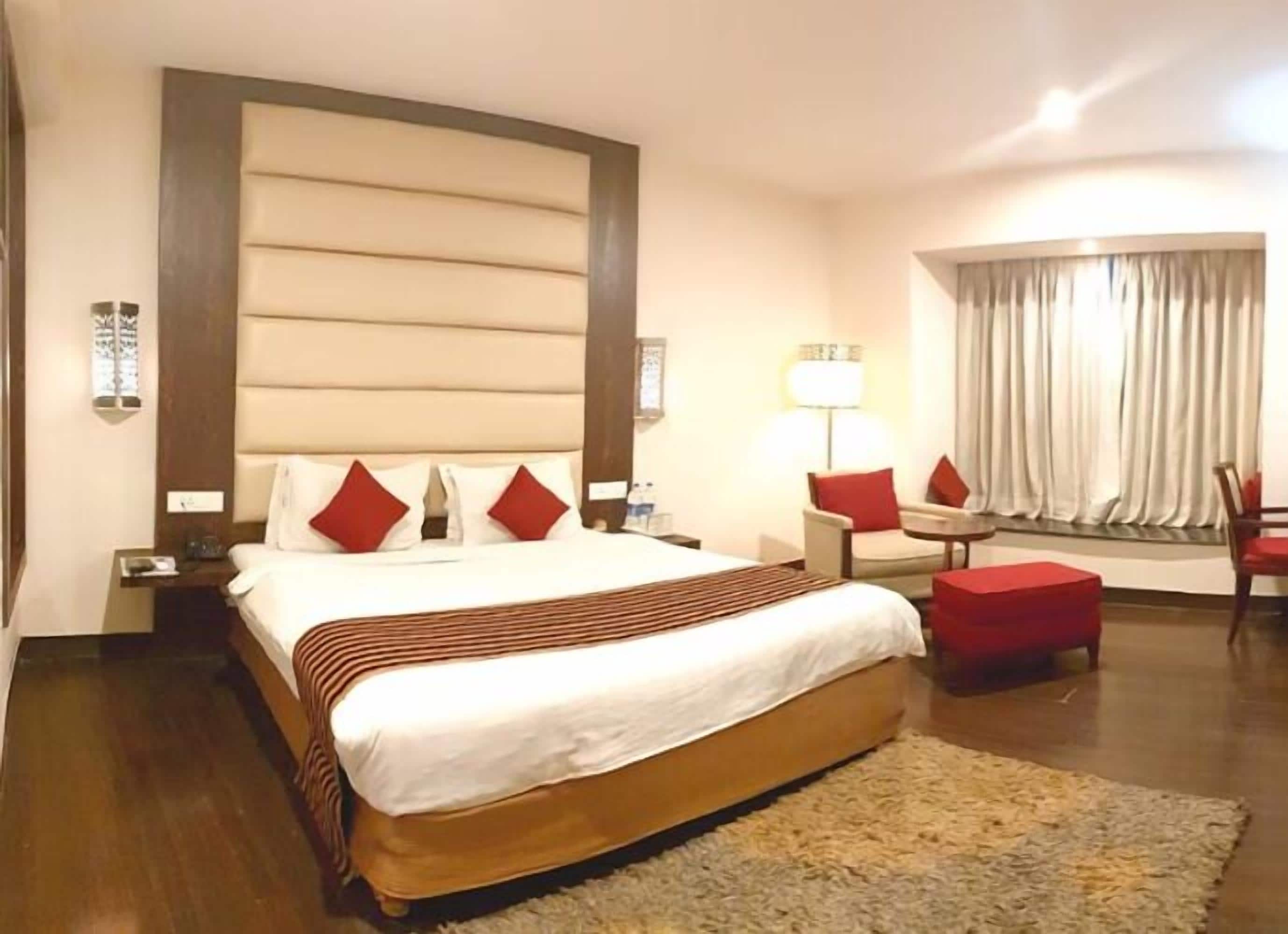 A hotel room with a large bed, a desk, a chair, a lamp, and a window with curtains.