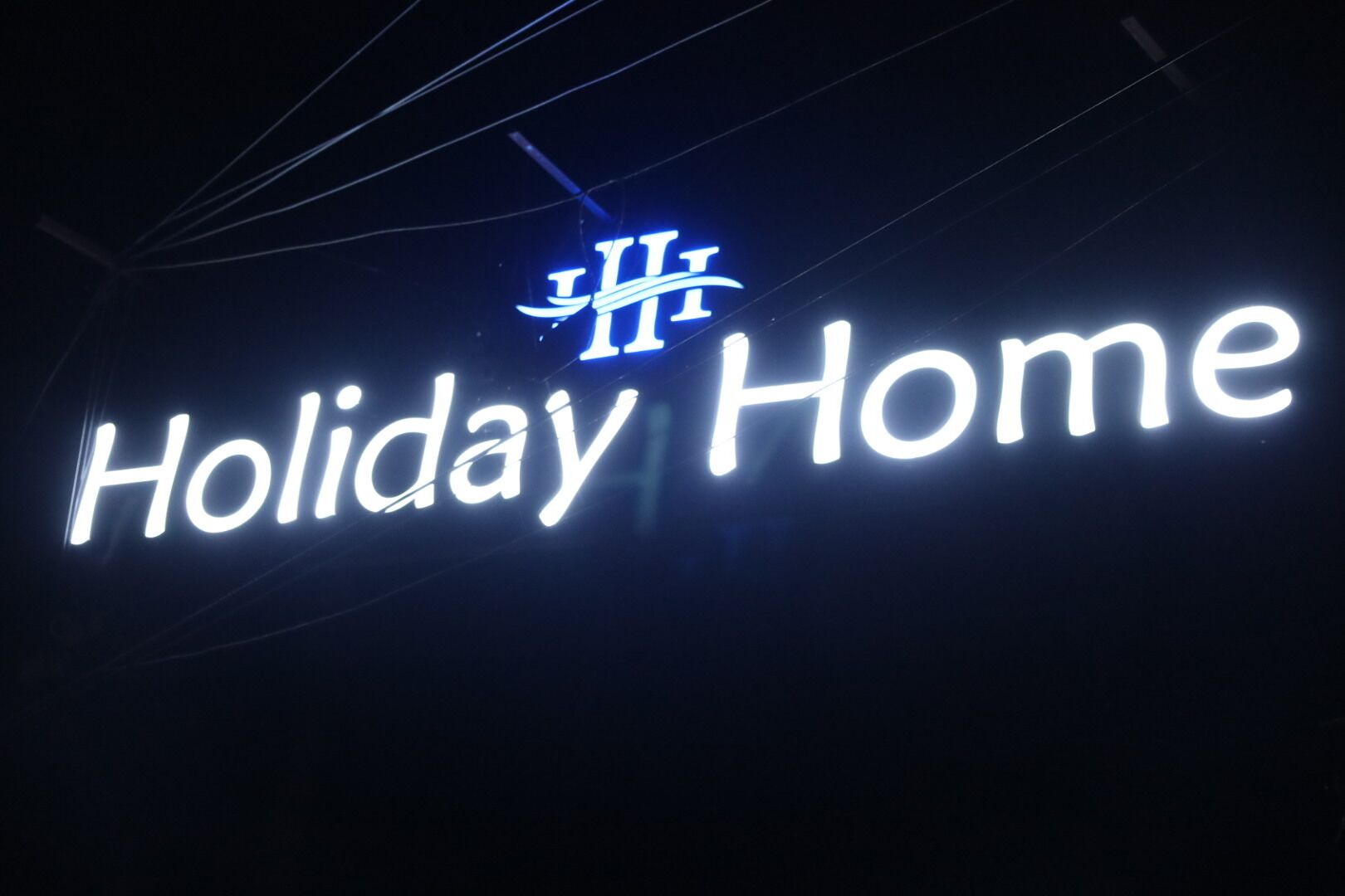 Un cartell de neó amb la frase 'Holiday Home' i un logotip a dalt.