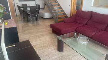 Una sala de estar con una mesa de centro de vidrio, un sofá rojo, un comedor con sillas y una escalera.