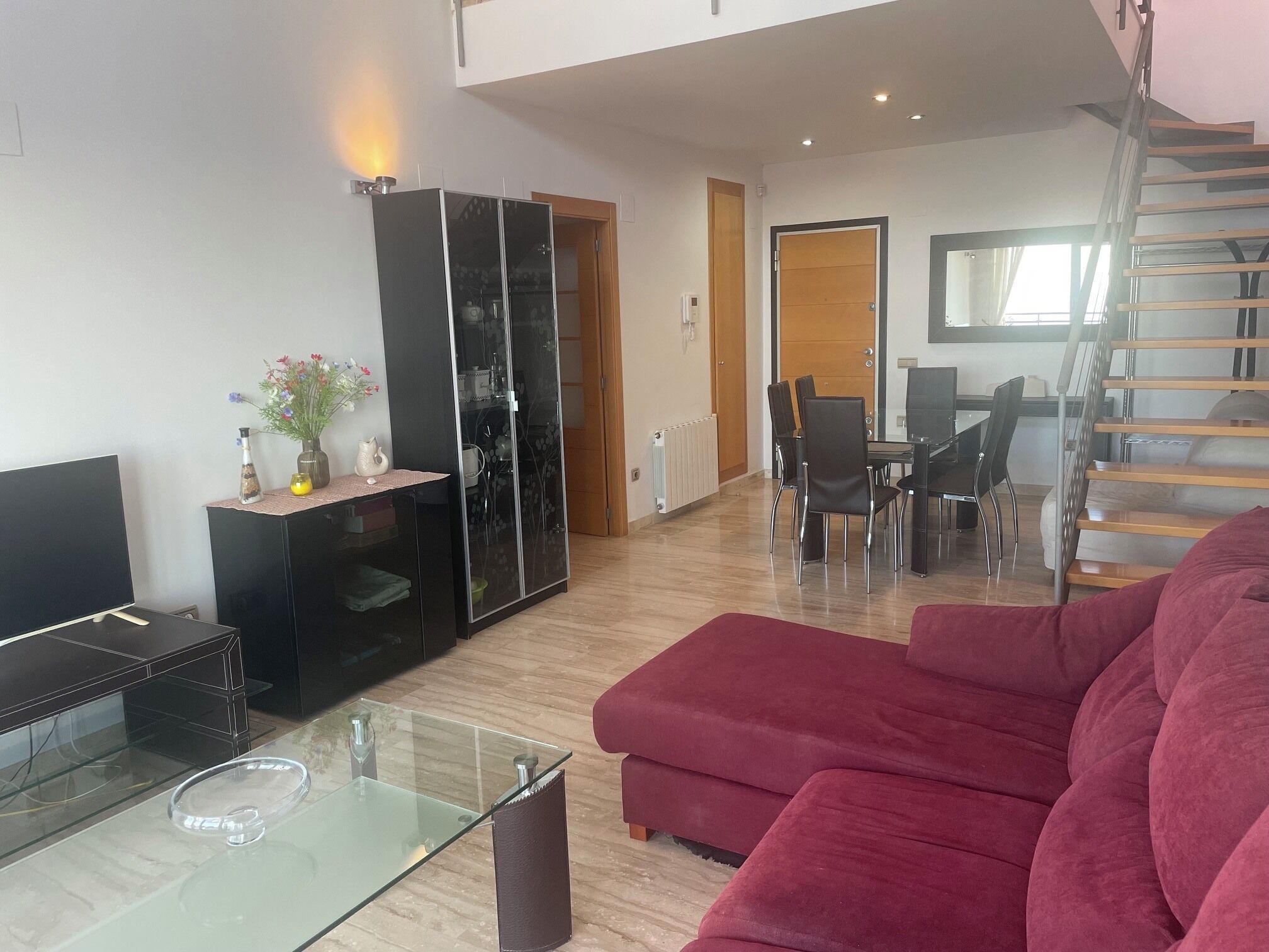 Un salon moderne avec une table basse en verre, un canapé rouge, un meuble de rangement noir et un coin repas comprenant des chaises et une table.