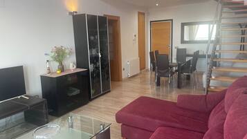 Un salon moderne avec une table basse en verre, un canapé rouge, un meuble de rangement noir et un coin repas comprenant des chaises et une table.