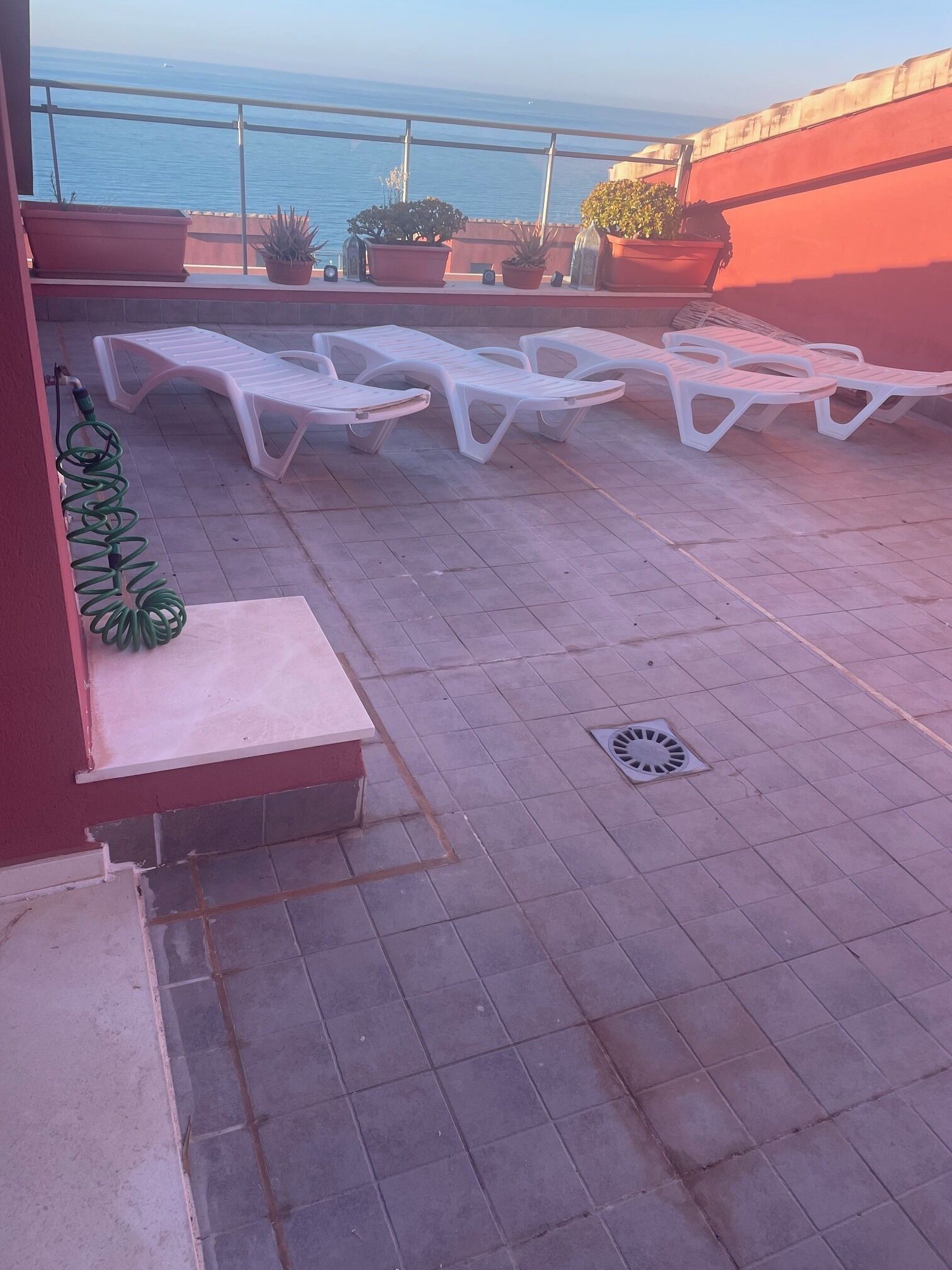 Una terraza con sillones blancos, plantas en macetas y vistas al mar.