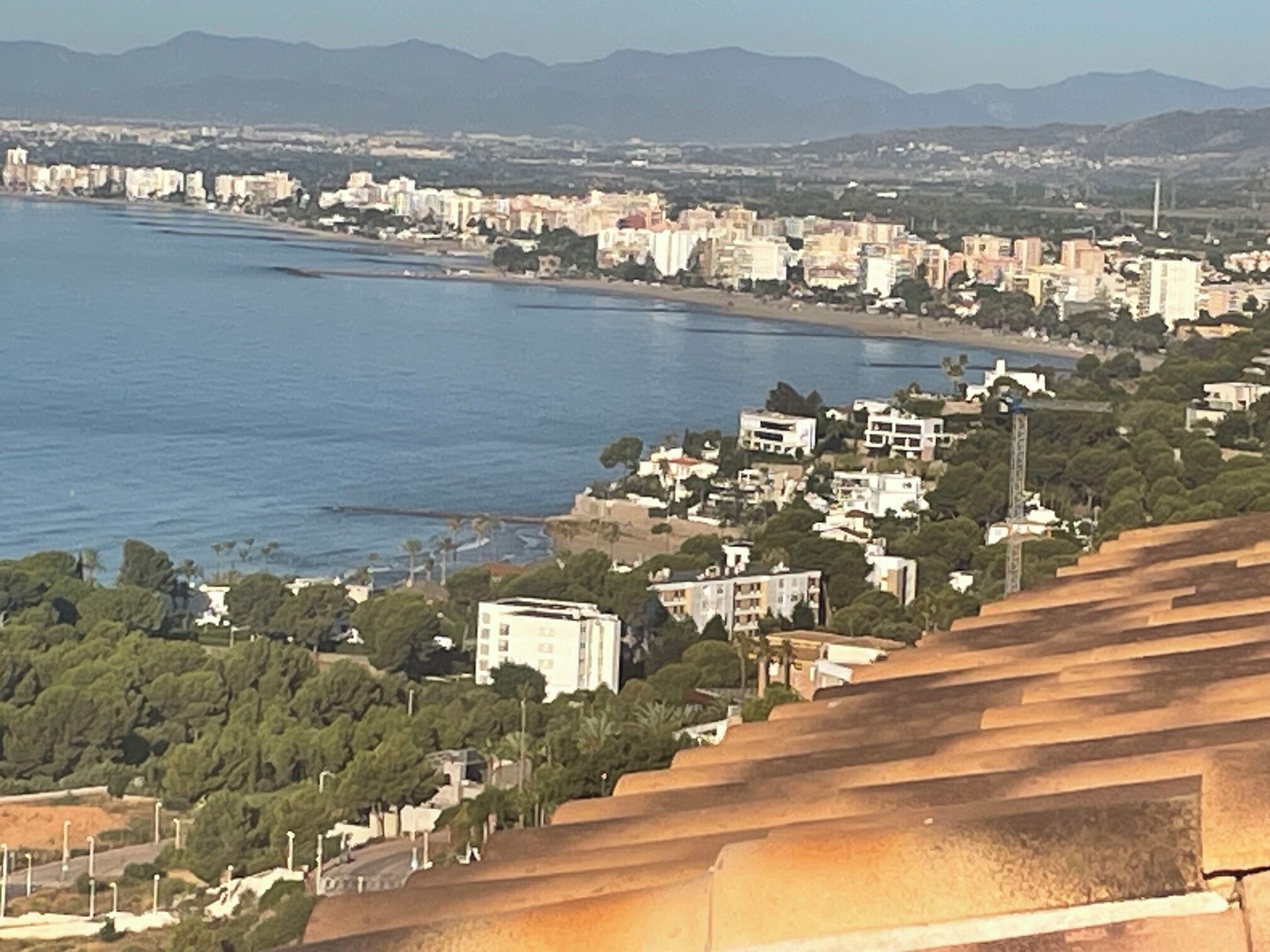 Un paisaje costero con edificios, una playa y montañas al fondo.