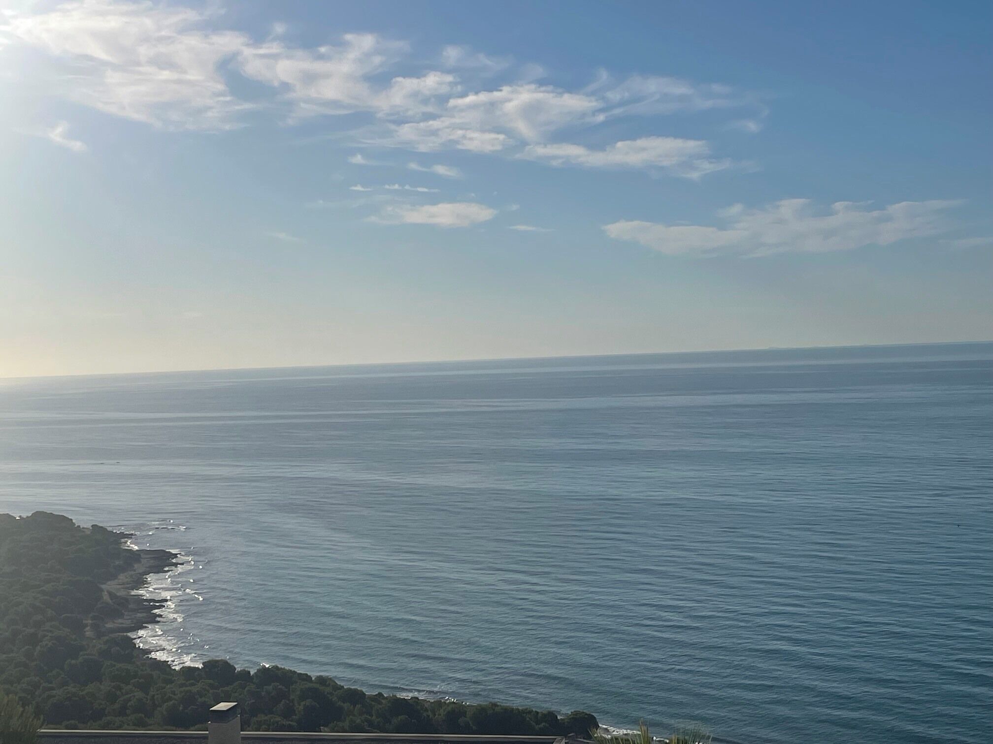 A coastal view with a clear sky, calm sea, and a distant shoreline.