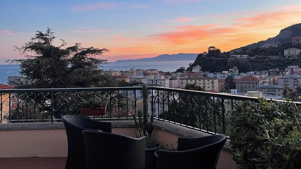 Ein Balkon mit Gartenmöbeln, Blick auf das Meer und Gebäude in der Ferne.