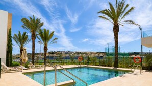 Une piscine bordée de palmiers, une vue sur la mer et un paysage lointain.
