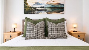 Une chambre à coucher avec un lit, deux tables de chevet, deux lampes, un tableau représentant un paysage et deux oreillers.