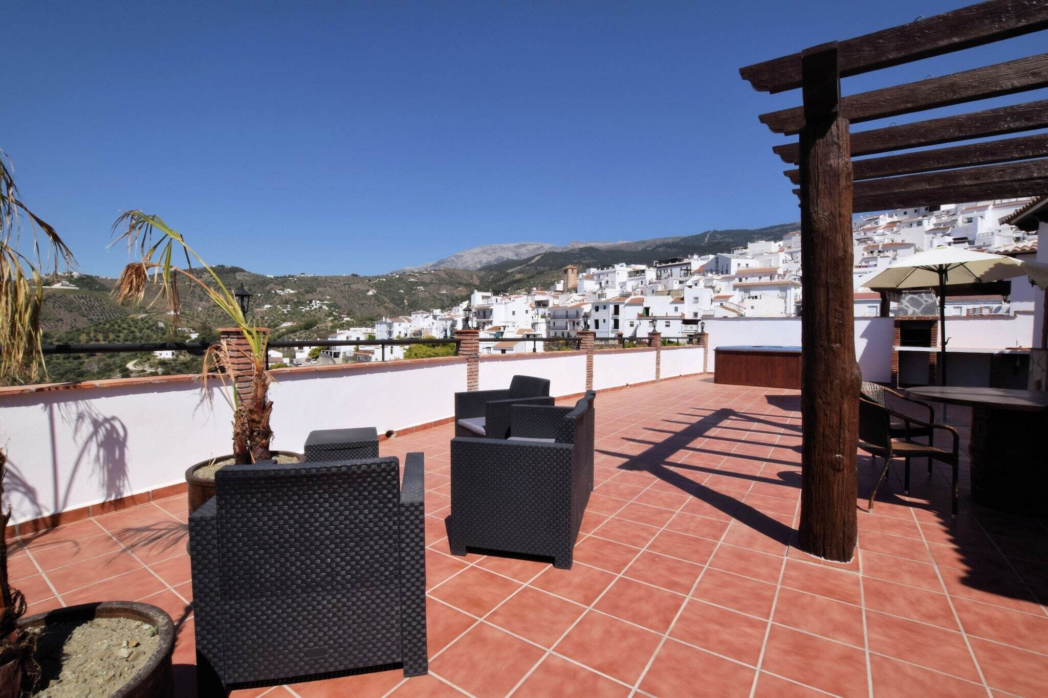 Une terrasse aménagée avec du mobilier d’extérieur, une pergola et une vue sur un village aux maisons blanchies à la chaux.