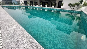 Une piscine dont le bord est recouvert de carreaux, entourée d’un bâtiment à toit plat et agrémentée de plantes en pot.