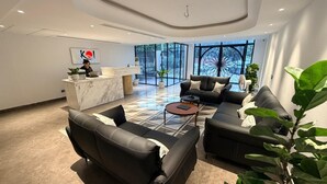 Un hall d’hôtel moderne avec un comptoir d’accueil, des canapés en cuir, un tapis à motifs et de grandes fenêtres offrant une vue dégagée.