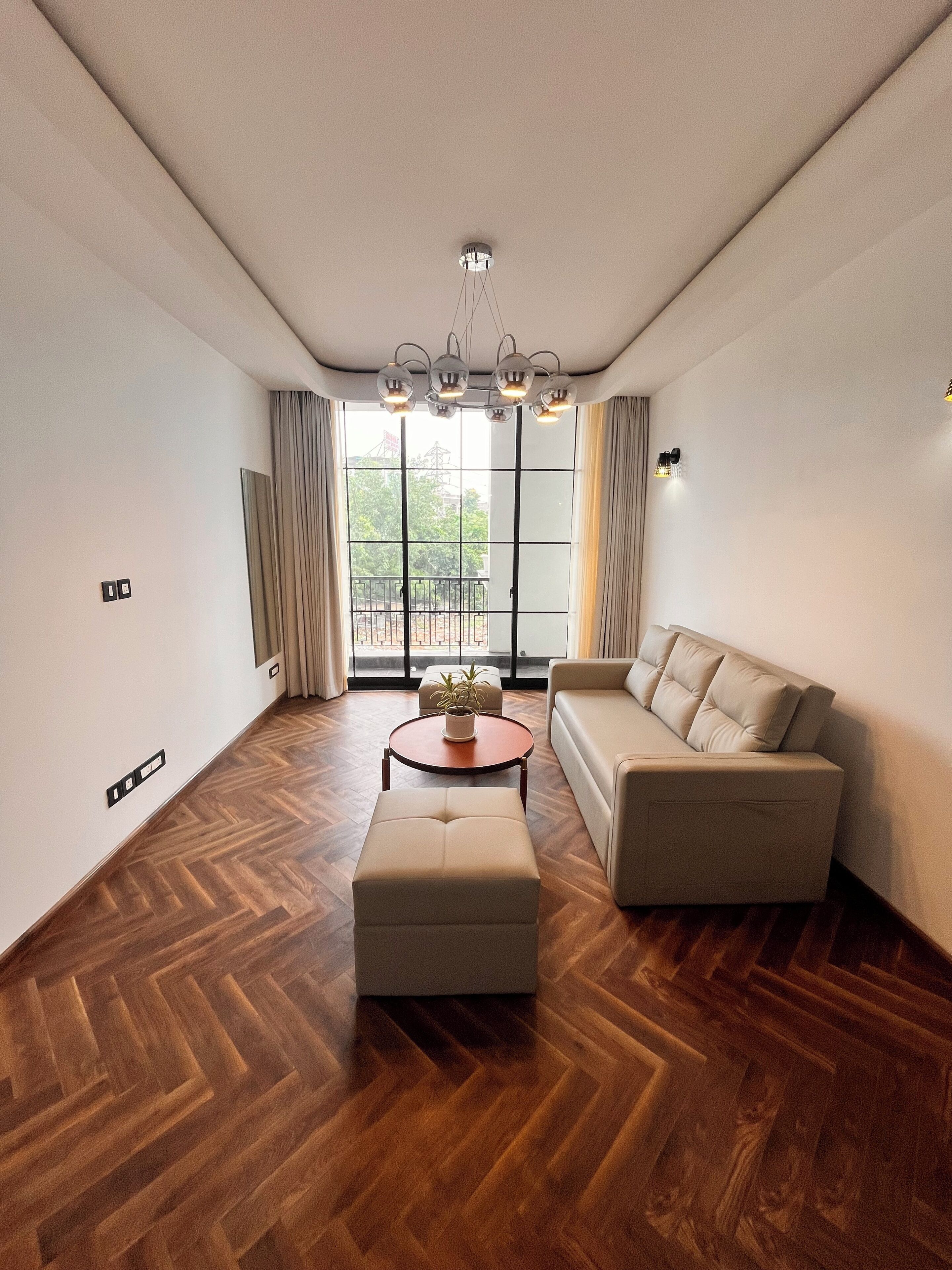 A modern living room with a herringbone floor, a sofa, a coffee table, and a chandelier.