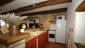 Una cocina con pared de piedra, vigas de madera, un refrigerador blanco y una estufa.