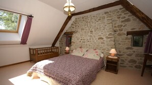 Un dormitorio con pared de piedra inclinada, una cuna de madera, una cama con colcha estampada y dos lámparas de noche.