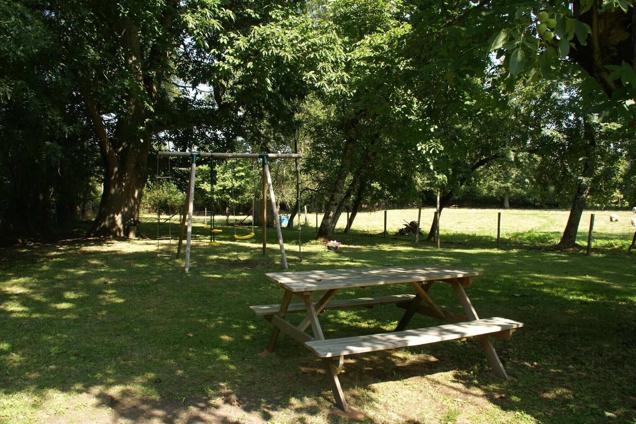 Un tavolo da picnic in un parco, con alberi e un'altalena sullo sfondo.