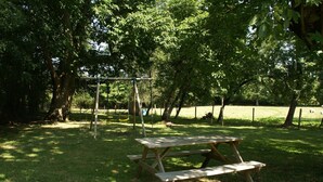Una mesa de picnic en un parque, con árboles y un columpio al fondo.