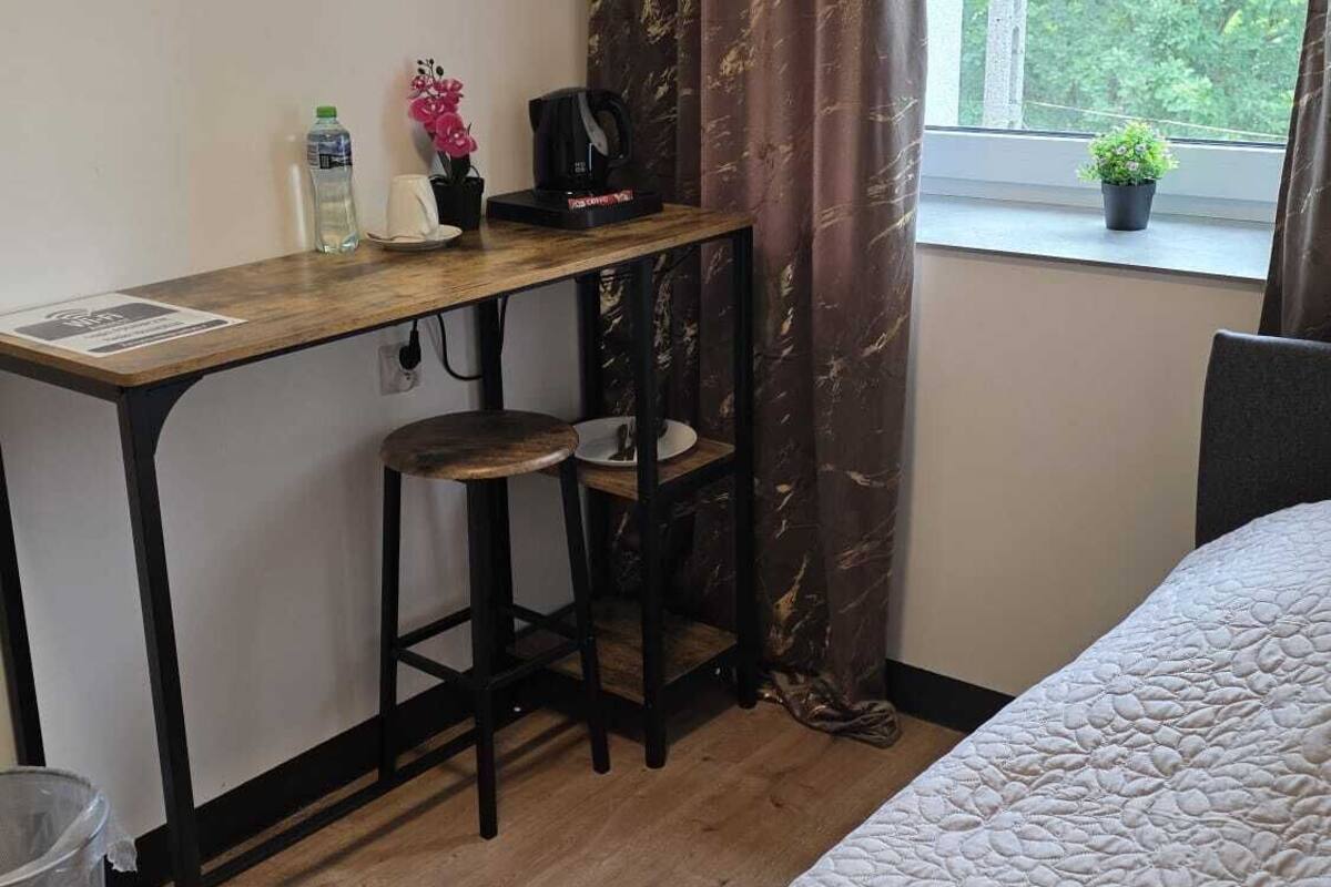 Een slaapkamer met een bed, een bureau met stoel, een raam met uitzicht op groen, en een gordijn.