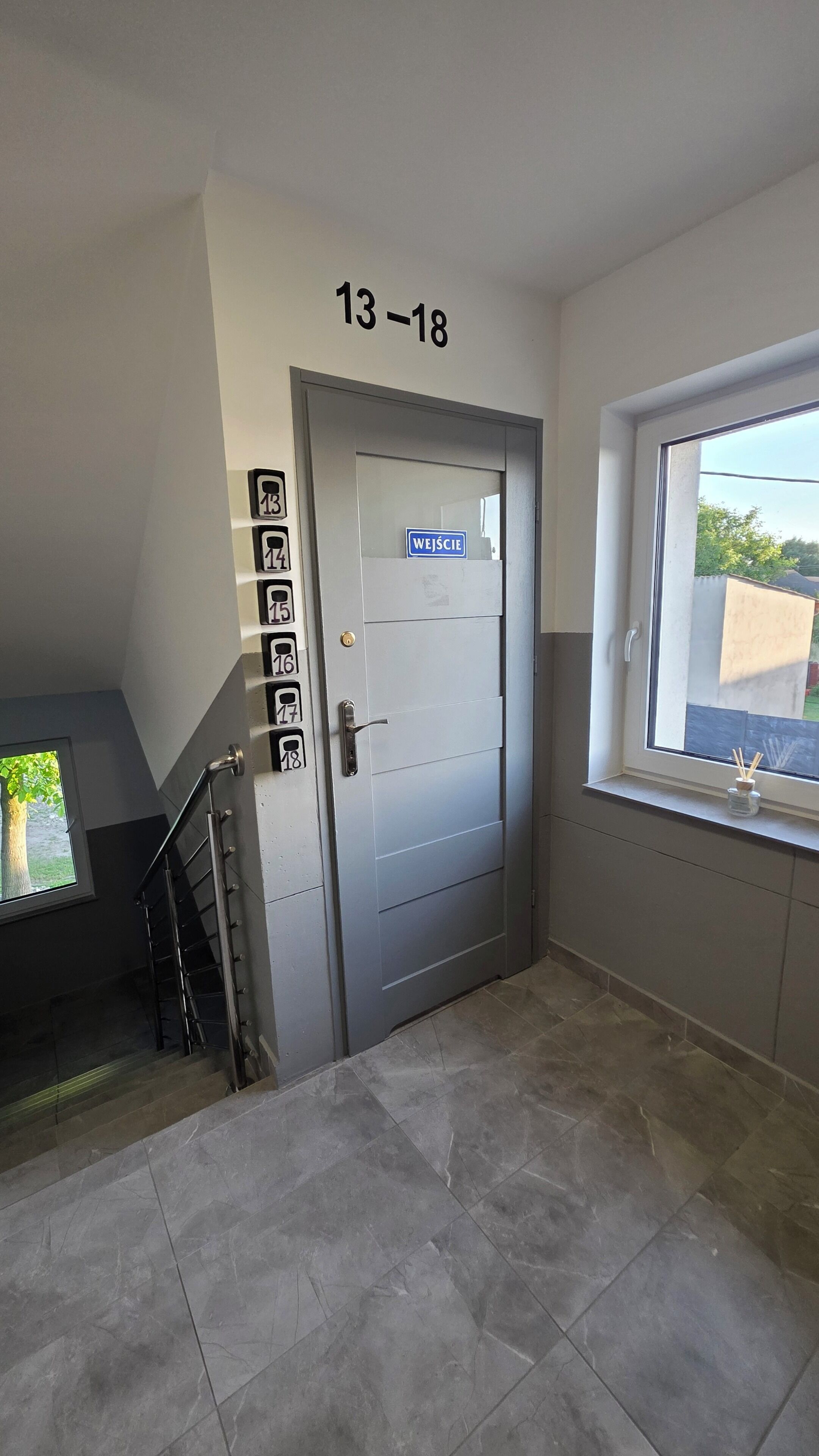 A stairwell with a door marked '13-18', a window with a view, and a small table with a bottle.