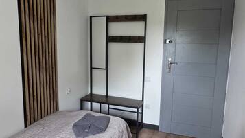 A bedroom with a bed, a wooden slat wall, a metal bed frame, a door, and a small table.