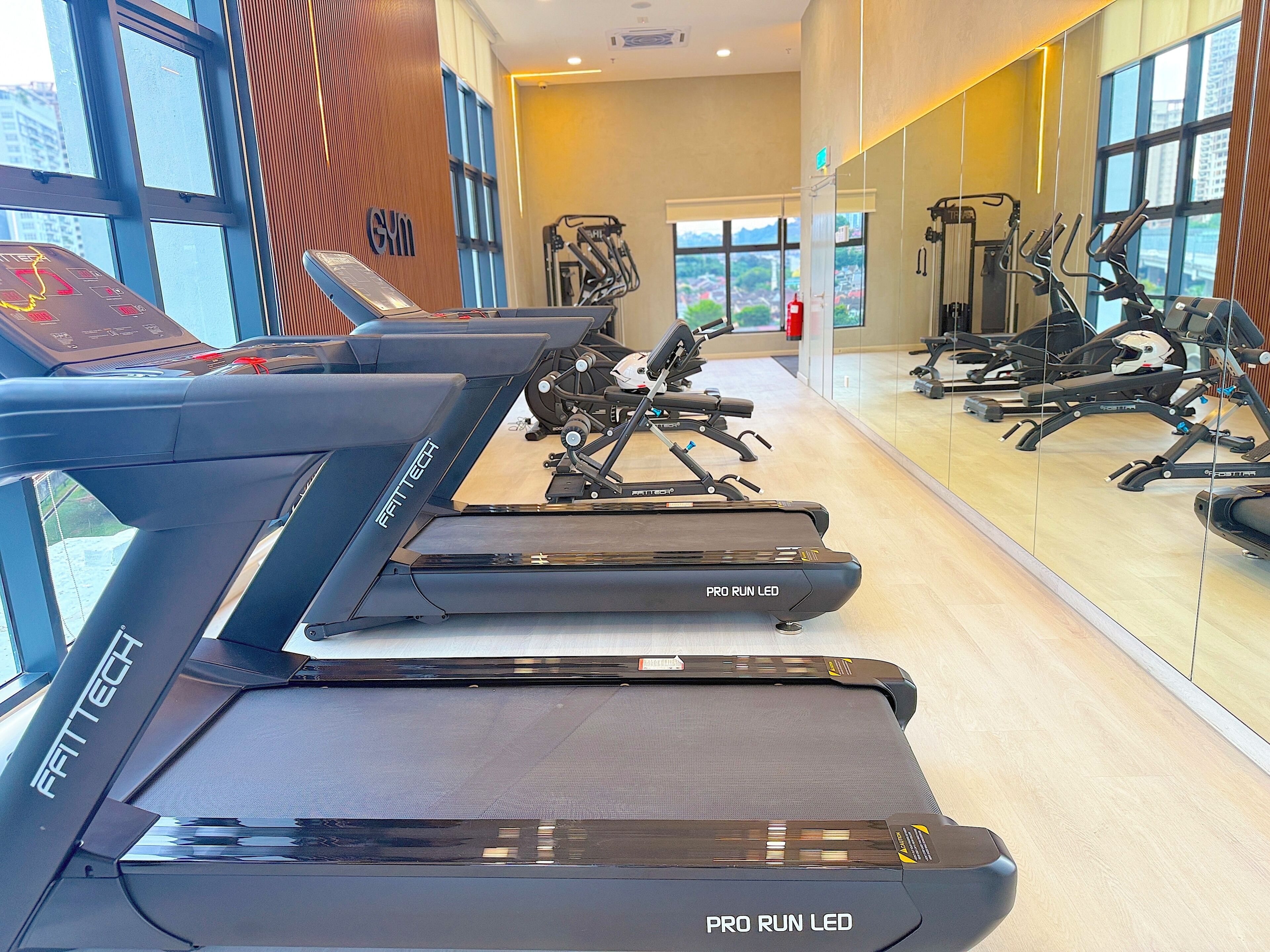 Un gimnasio con cintas de correr, bicicletas estáticas y un amplio ventanal con vista a la ciudad.
