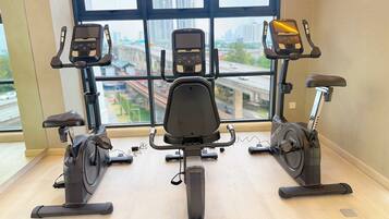A gym with three stationary bikes, a central rowing machine, and a large window with a city view.