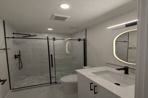 A modern bathroom with a glass-enclosed shower, a white sink, and a mirror with a circular light. - Modern 2-Bedroom 2-Bath Basement Suite in Aspen (Calgary)