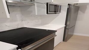 Een keuken met een zwart inductiekookveld, een roestvrijstalen koelkast en een magnetron boven het aanrecht.