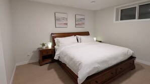 Een slaapkamer met een houten bed, wit beddengoed, twee nachtkastjes met lampen en een raam.