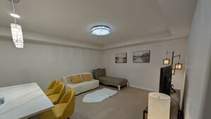 Een gezellig ingerichte leefruimte met een eettafel, gele stoelen, een bank, een televisie en een lamp.