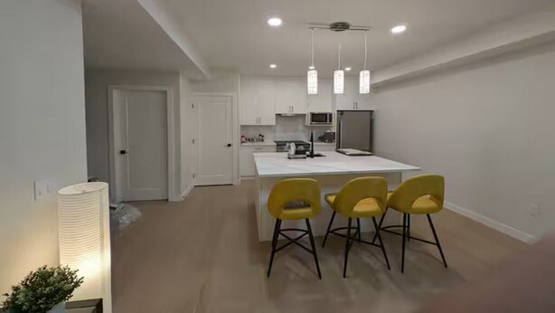 Een moderne keuken met witte kasten, een wit kookeiland en een magnetron. Rond het eiland staan drie gele stoelen.