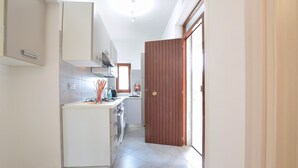Una cuina estreta amb armaris blancs, un forn integrat i una porta de fusta.