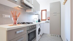 Cuina compacta amb fogó a gas, forn, rentadora i una petita finestra.