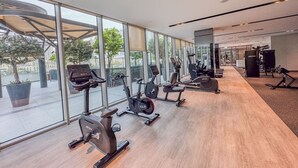 Un gimnasio con máquinas de cardio, estaciones de pesas y grandes ventanales que ofrecen vistas al exterior.