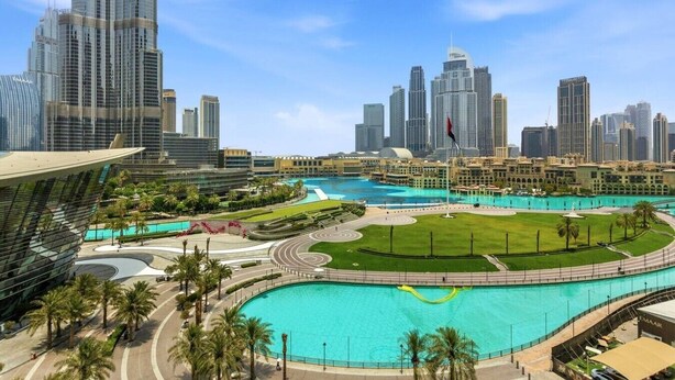 Un paisaje urbano moderno con edificios altos, una piscina central y palmeras.