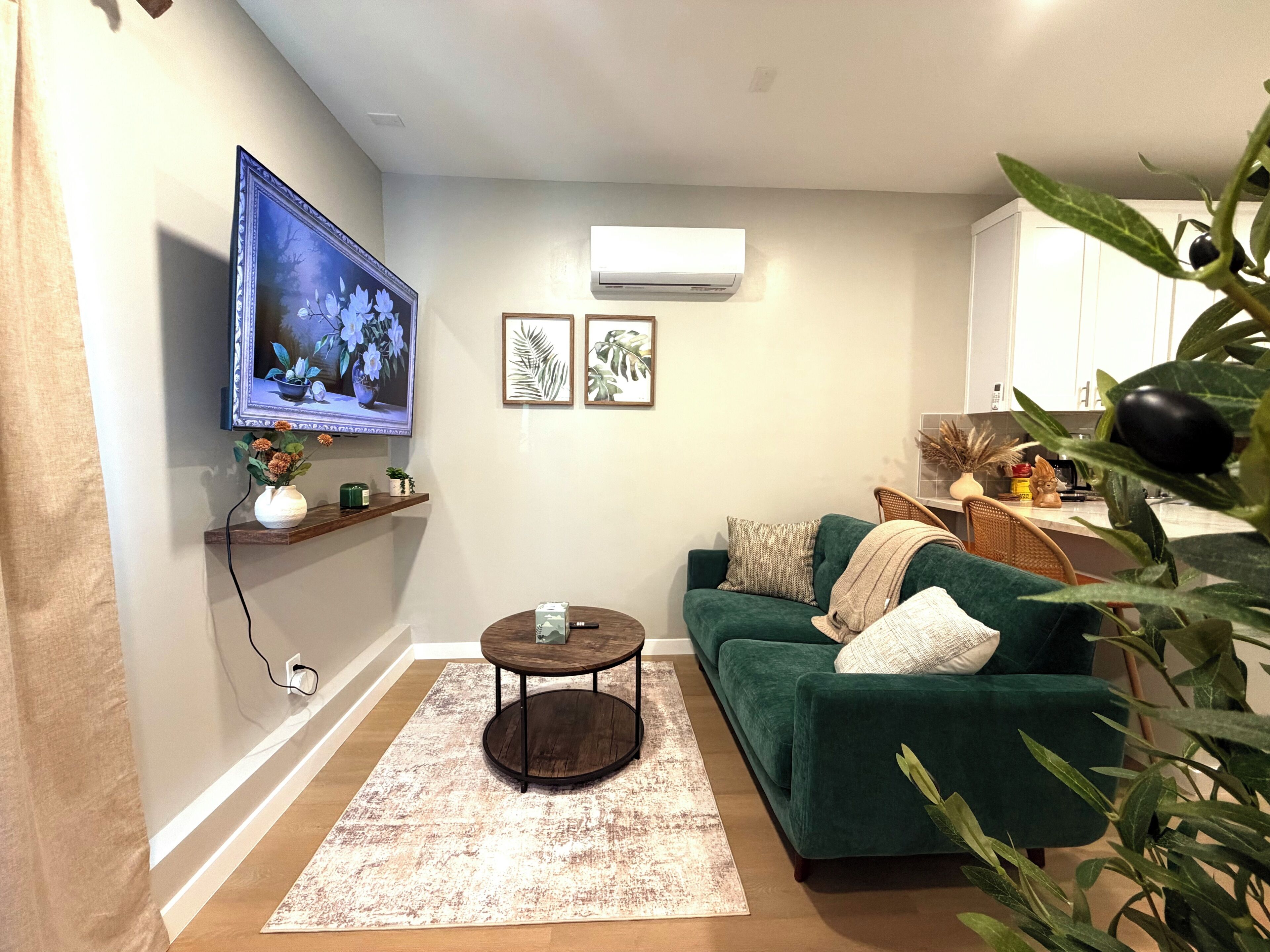 A living room with a green sofa, a coffee table, a TV mounted on the wall, and framed artwork.