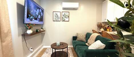 A living room with a green sofa, a coffee table, a TV mounted on the wall, and framed artwork.
