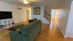 A living room with a green sofa, a flat-screen TV, and a ceiling fan.