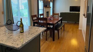 A dining area with a marble countertop, wooden chairs, a table, and a bottle of wine.