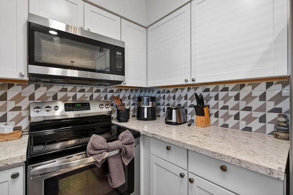 Una cocina con armarios blancos, microondas, estufa, cafetera y tostadora.