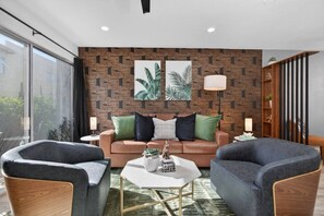 A modern living room with a brown patterned wall, a brown sofa, two armchairs, a coffee table, and two floor lamps. - Walk to Fashion Square & Old Town | Heated Pool (Scottsdale)