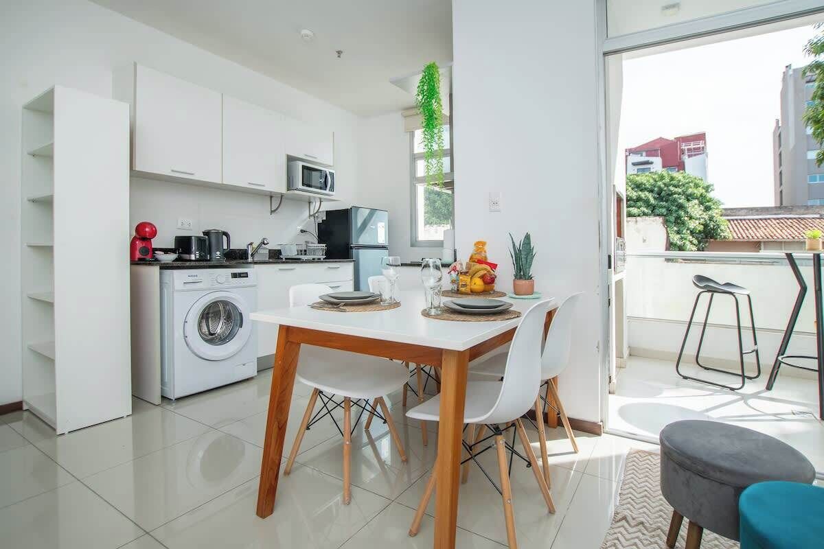 A modern kitchen with a washing machine, microwave, and dining area with chairs and a table.