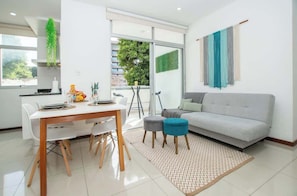 Una sala de estar moderna con una mesa de comedor, sofá y vistas al verdor exterior.